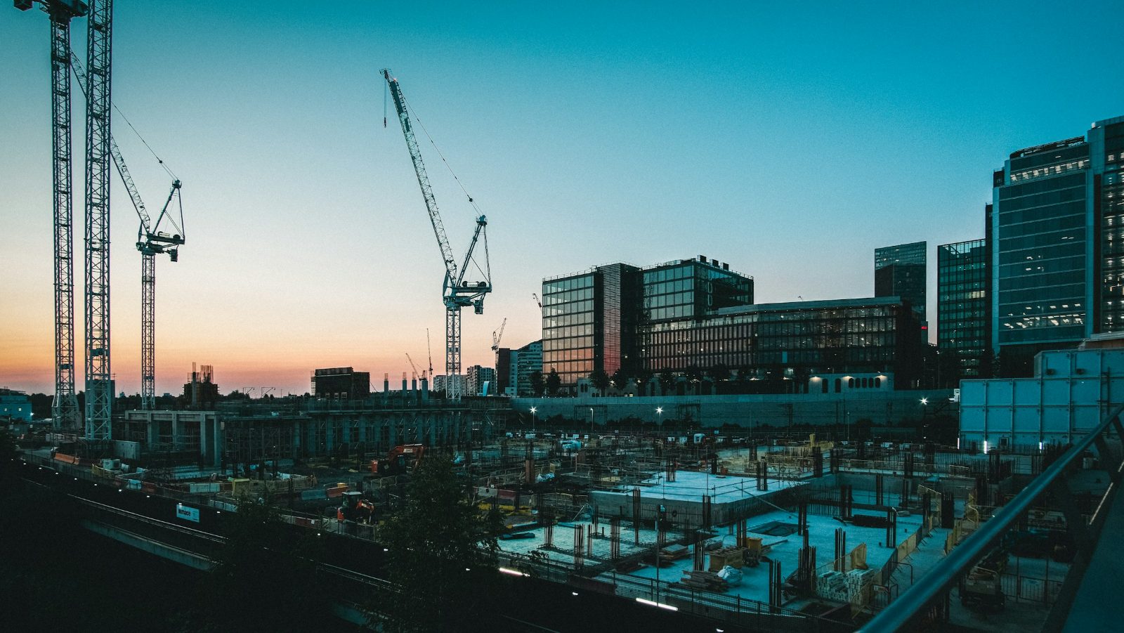 Construction site at dusk with tower cranes, concrete foundations and modern office buildings