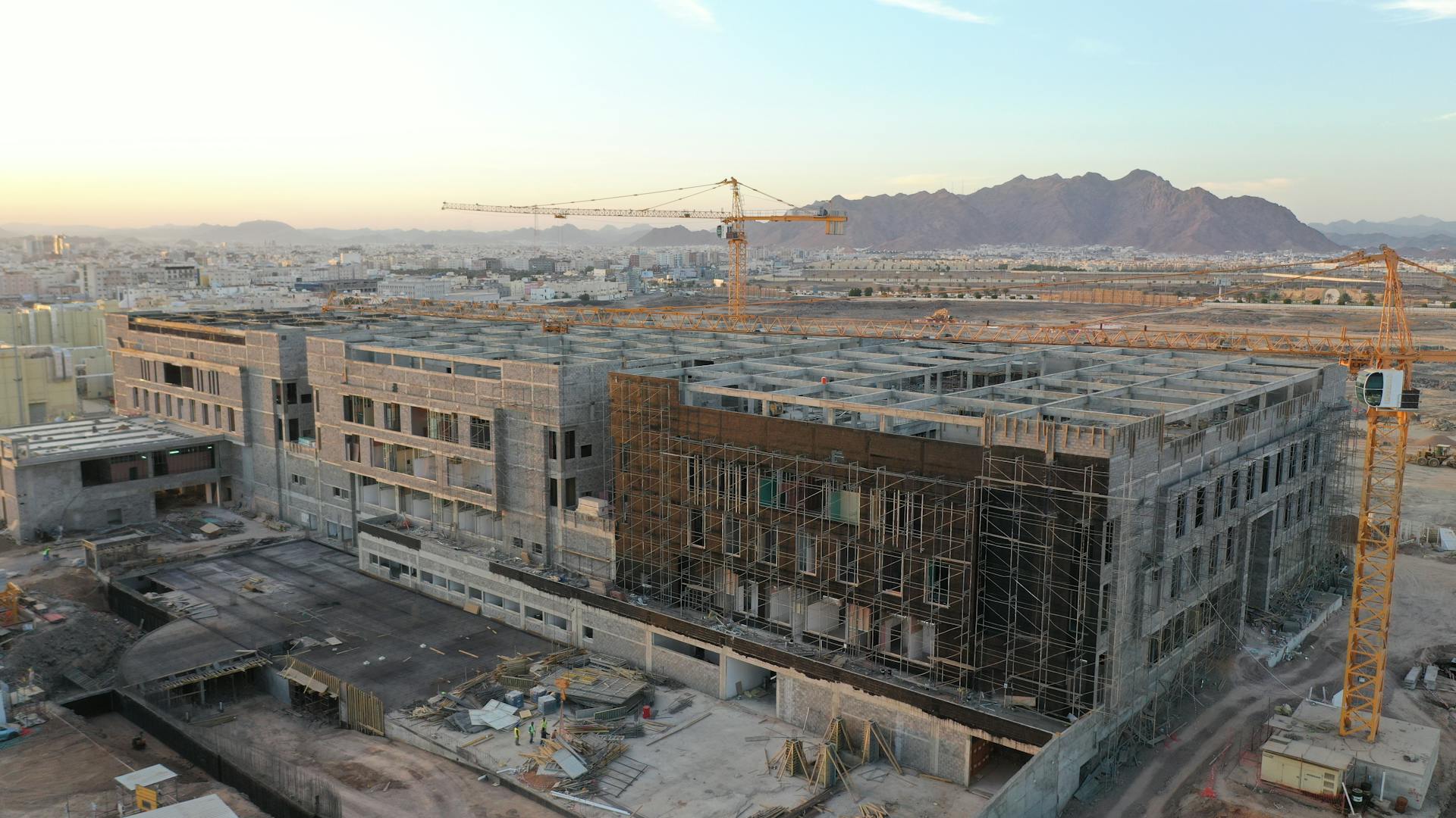Estrutura de uma edificação em construção com gruas e infraestrutura urbana ao fundo